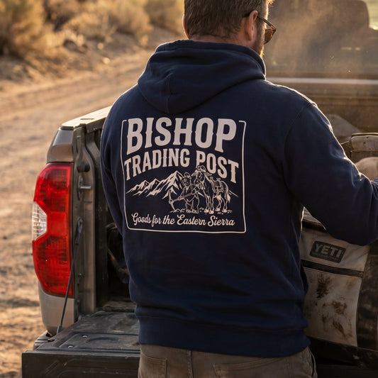 Person wearing a 'Bishop Trading Post' hoodie standing next to a truck in a desert setting
