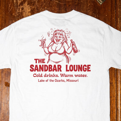 White t-shirt with red graphic and text on a wooden surface with vintage items.