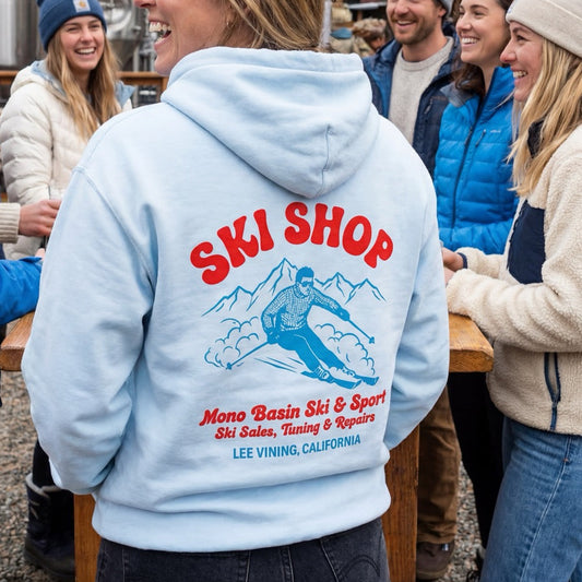 Person wearing a hoodie with 'Ski Shop' design in a snowy outdoor setting